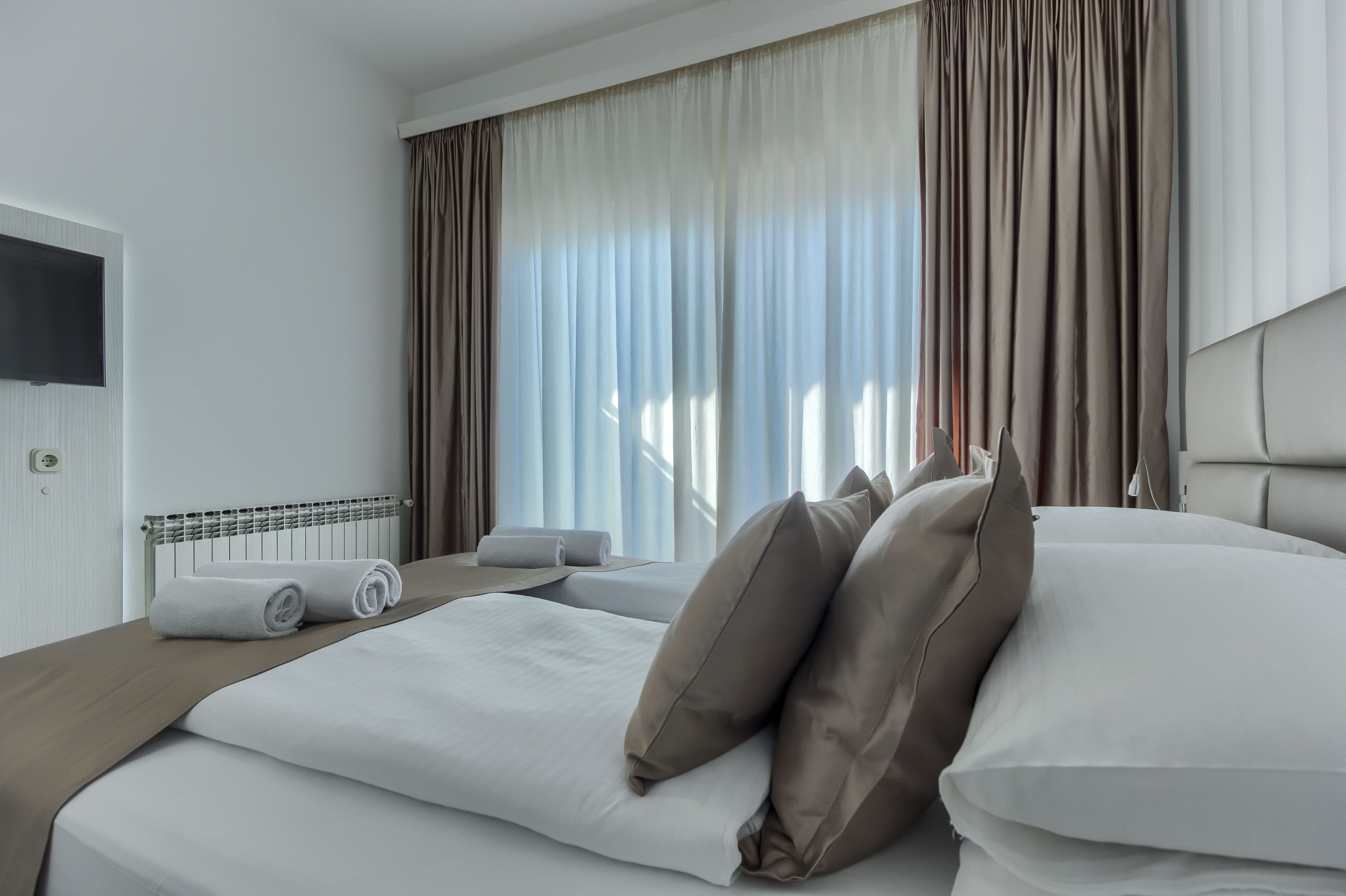 A hotel room with a bed, a TV, a radiator, and curtains.