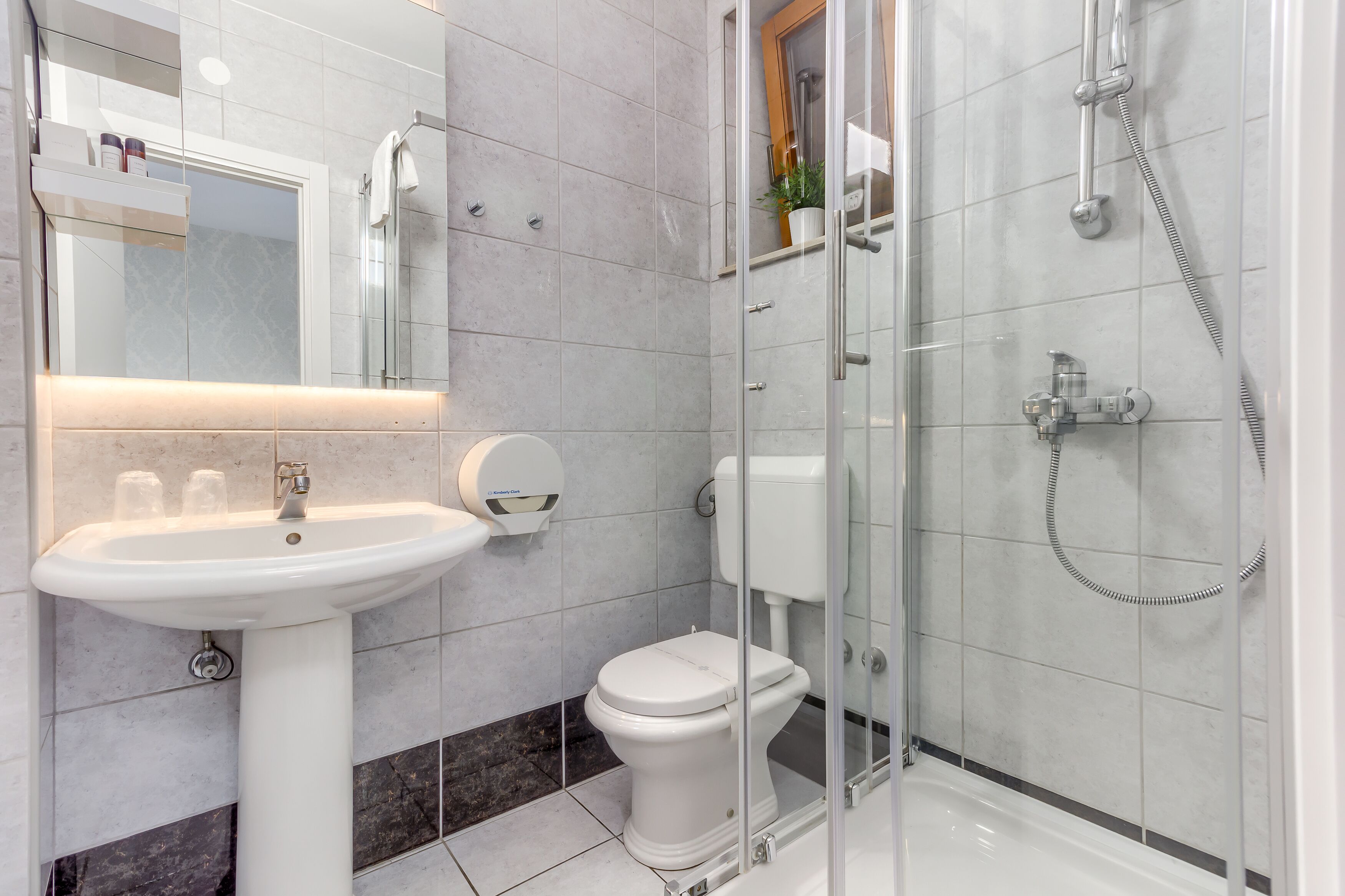 Un bagno moderno con doccia vetrata, lavabo su piedistallo e water.