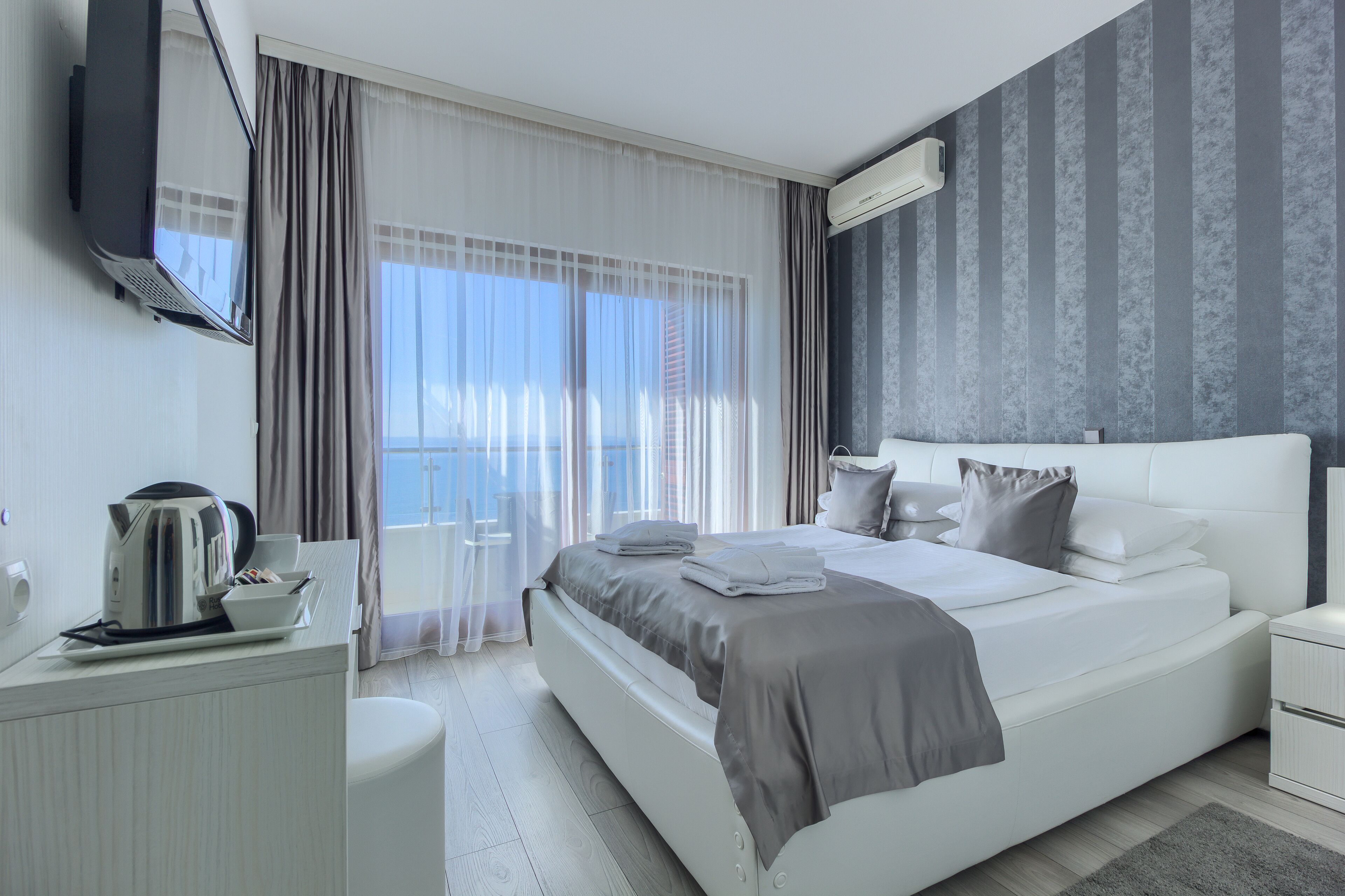 Habitación de hotel moderna con una cama grande, una mesita de noche, televisión de pantalla plana y vistas al exterior.