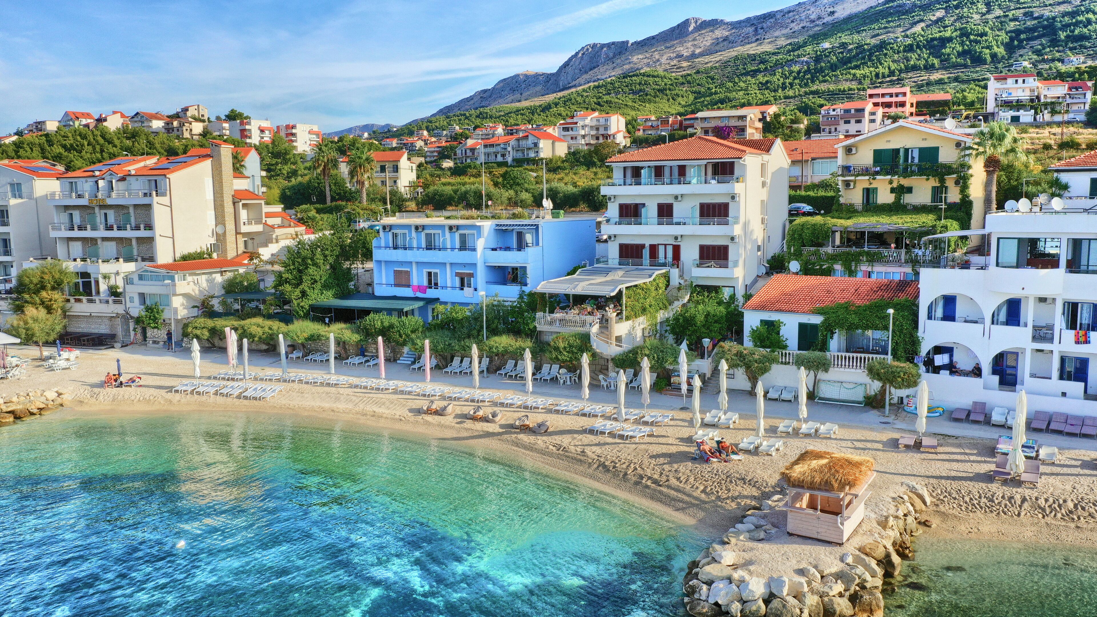 Un pueblo costero con playa, aguas cristalinas y edificios con techos de tejas rojas.