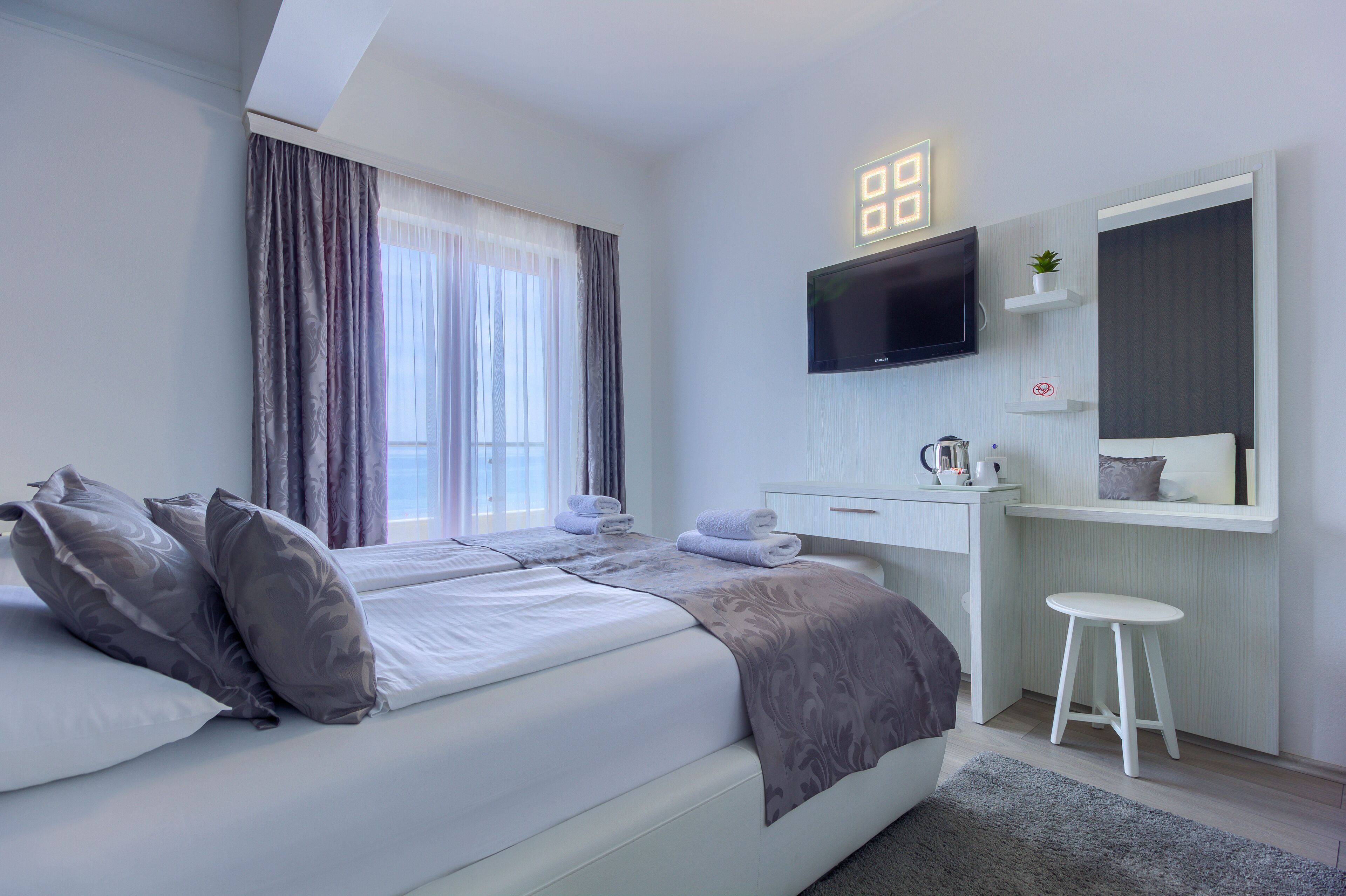 Una camera da letto moderna con un letto, una scrivania, una sedia, una televisione e una finestra con tende.