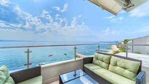 A balcony with a view of the sea, a sofa, and a glass table. - Pansion Martin (Podstrana)