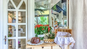 A room with a wooden table, a chocolate cake, a potted plant with red flowers, and a white lace tablecloth. - Pansion Martin (Podstrana)