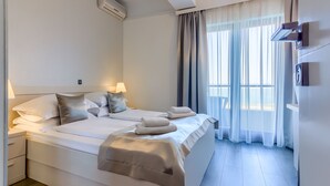 A modern hotel room with a large bed, bedside lamps, a built-in air conditioner, and a view of the sea through sheer curtains. - Pansion Martin (Podstrana)