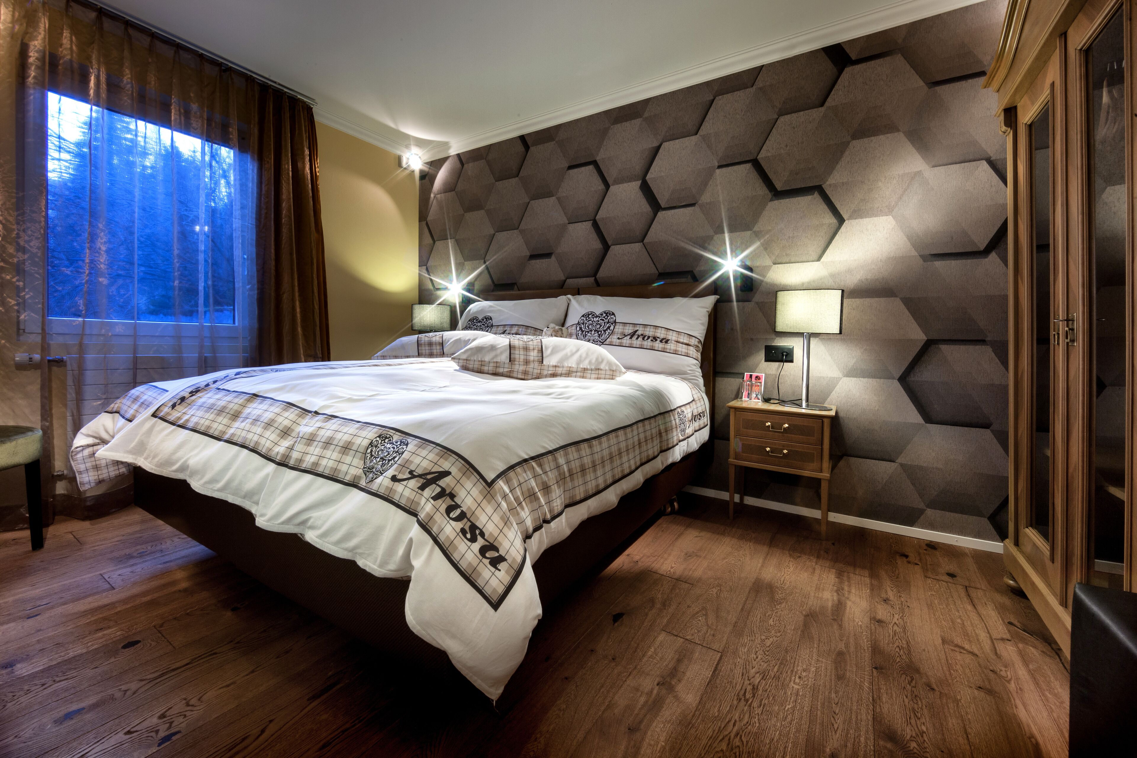 A bedroom with a large bed, a nightstand, a lamp, and a window with curtains.