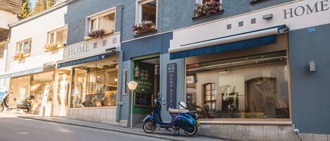 A building with a 'HOME HOTEL' sign, a storefront with mannequins, and a parked scooter.