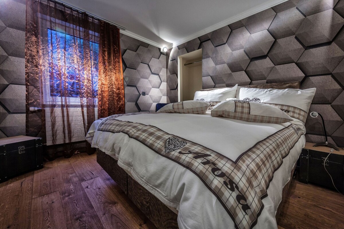 A bedroom with a large bed, a nightstand, a dresser, and a window with curtains.