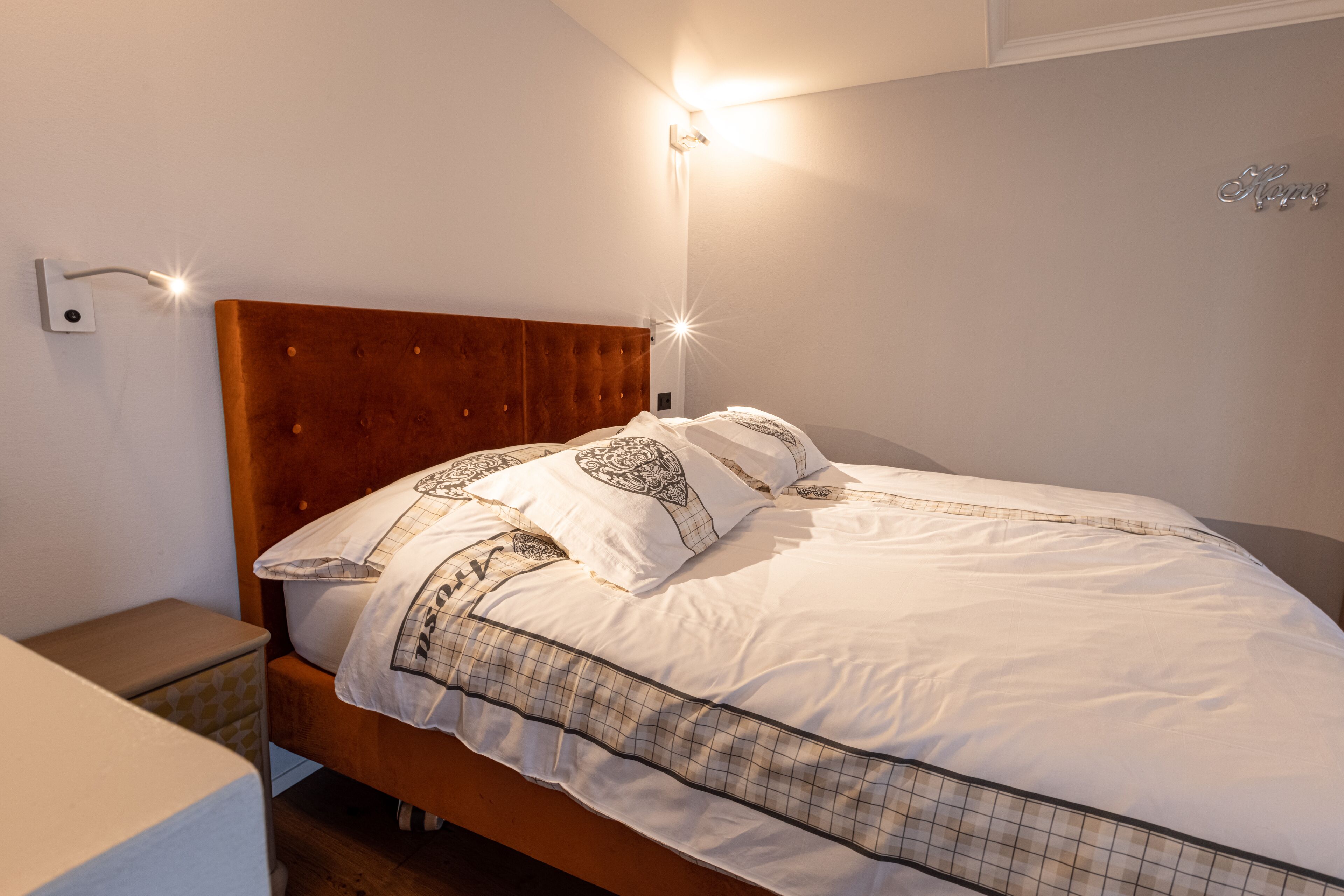 A neatly made bed with a wooden headboard, a bedside table, and a wall-mounted light fixture.