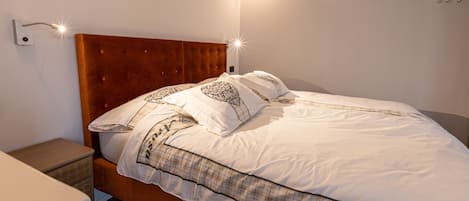 A neatly made bed with a wooden headboard, a bedside table, and a wall-mounted light fixture.
