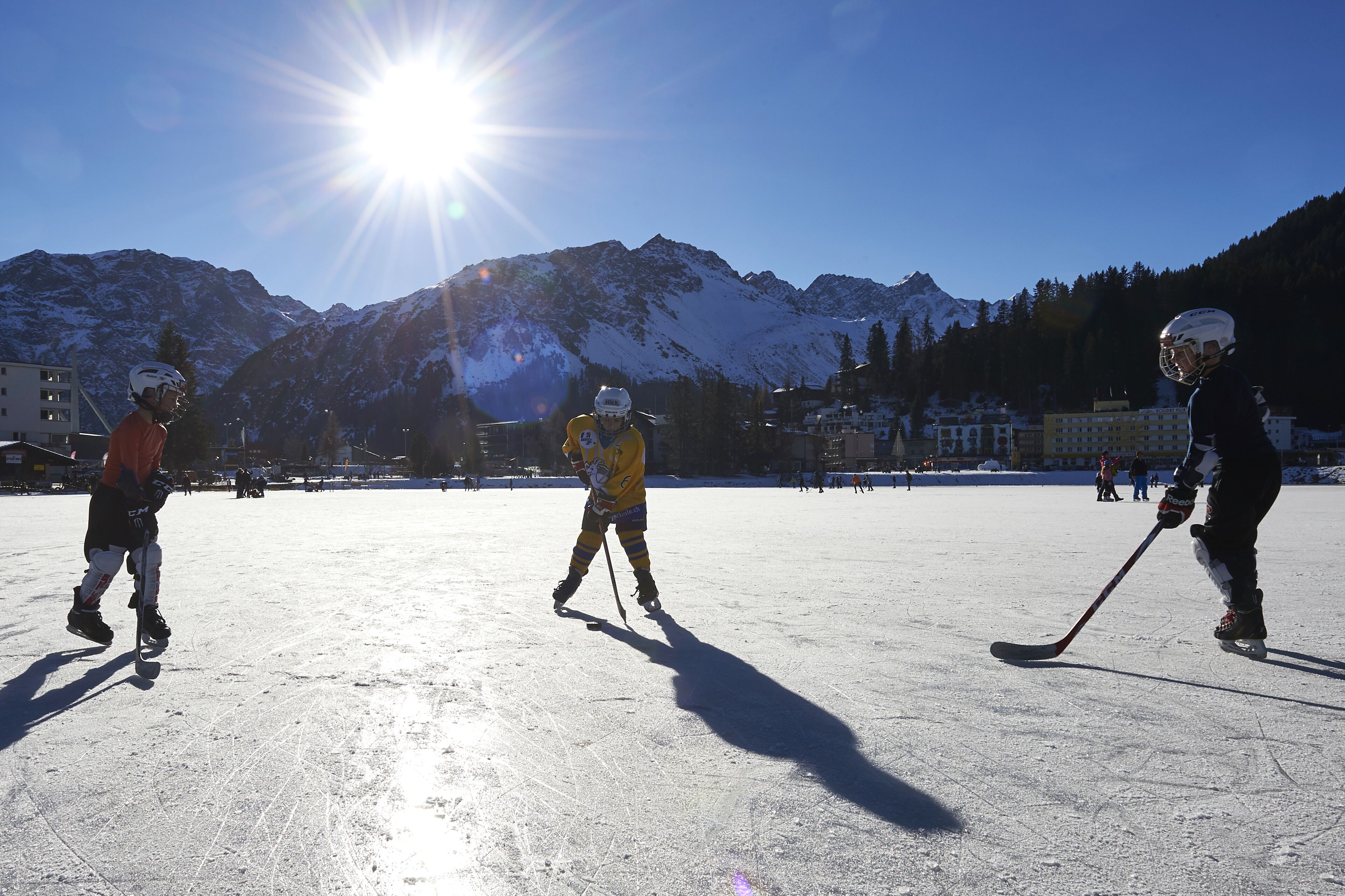 Een groep mensen schaatst op een zonnige dag, met bergen op de achtergrond.