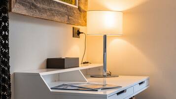 Een bureau met een lamp, een lijst met een schilderij en een paarse stoel.
