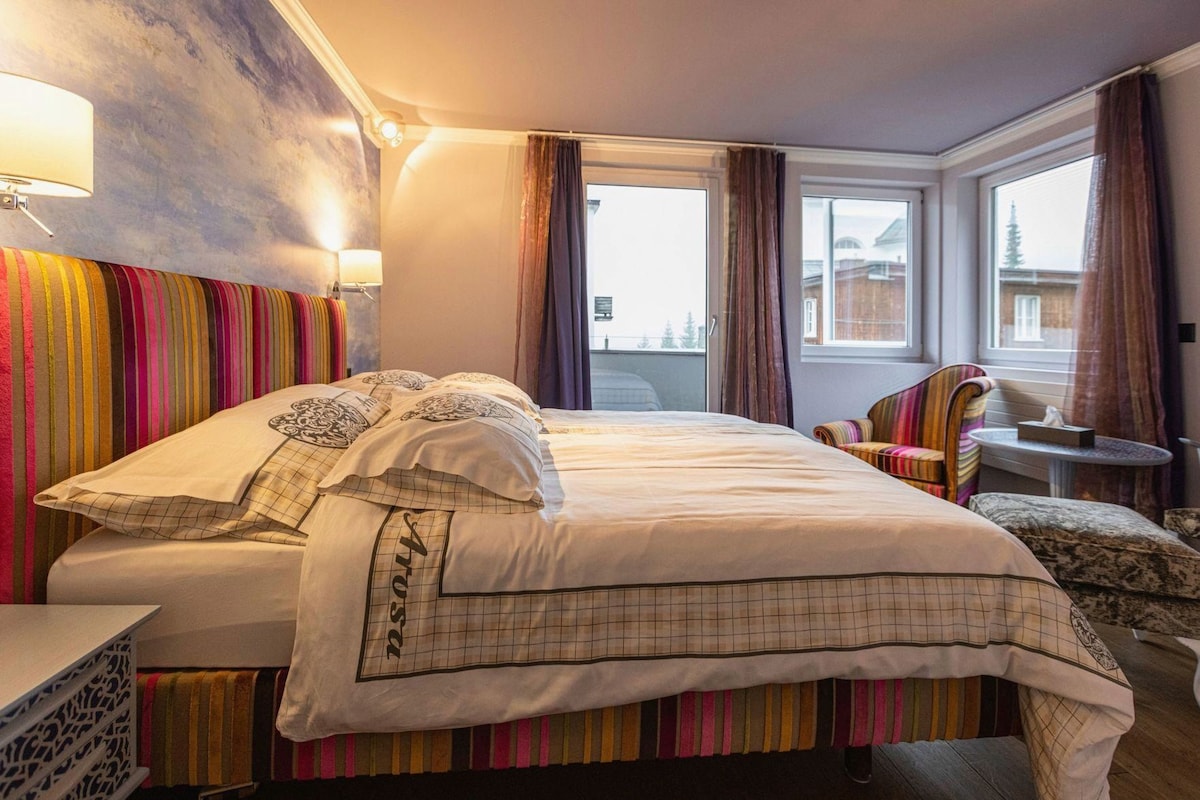 A hotel room with a bed, a chair, a small table, and a window.