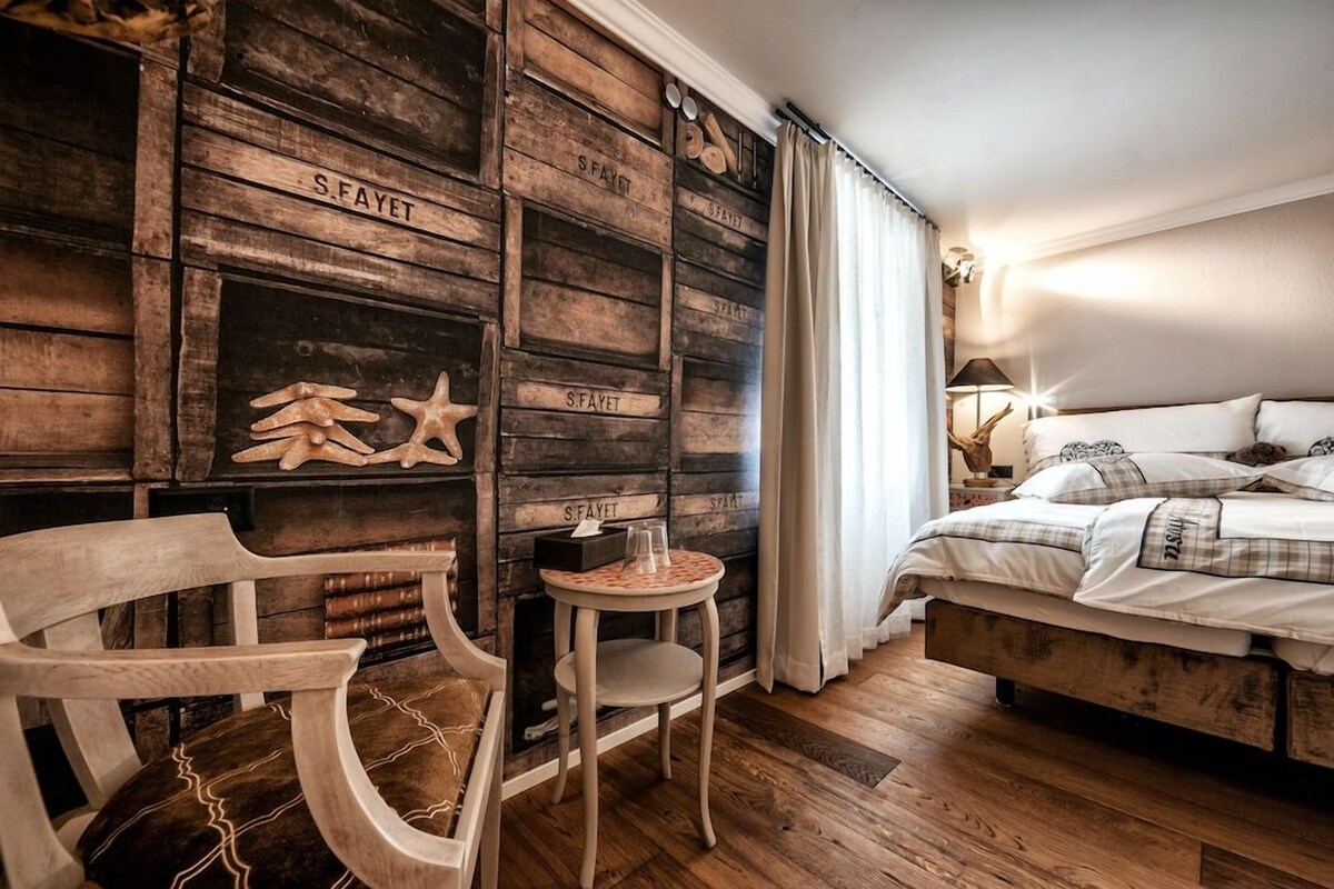 A bedroom with a wooden wall, a bed with white bedding, a small round table, and a chair.