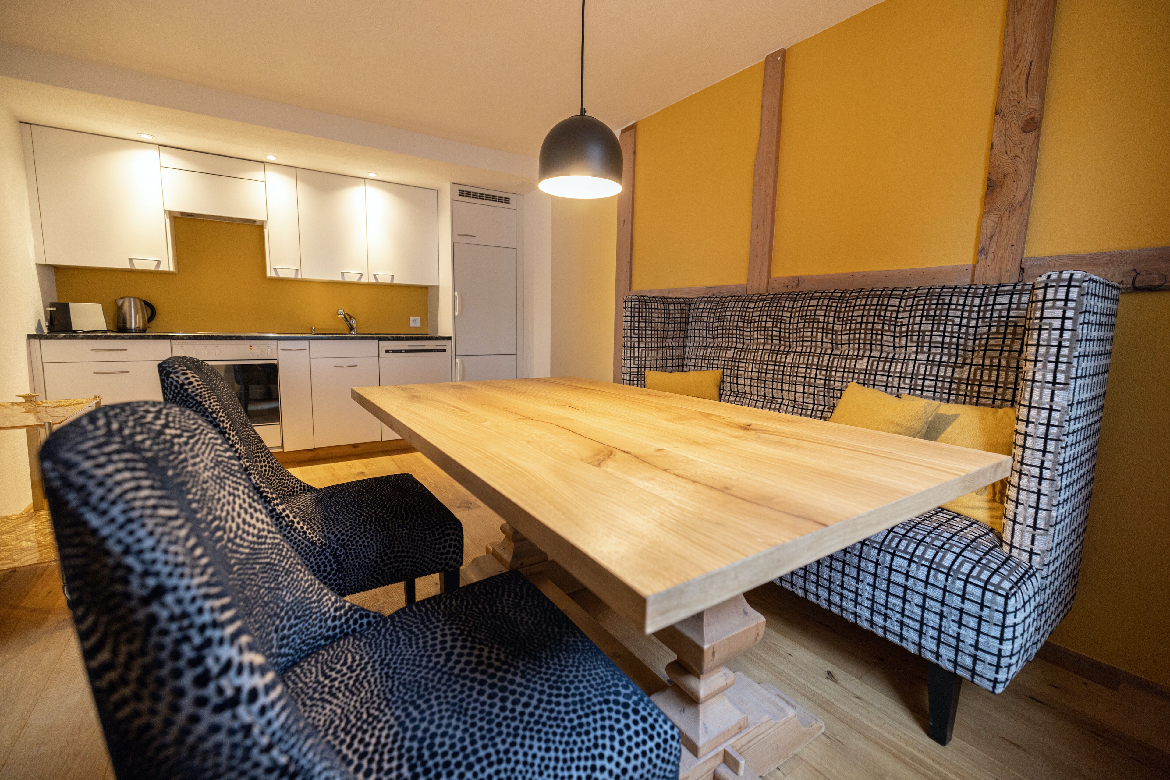 Une cuisine moderne avec des meubles blancs, une table à manger en bois et un banc à motifs.