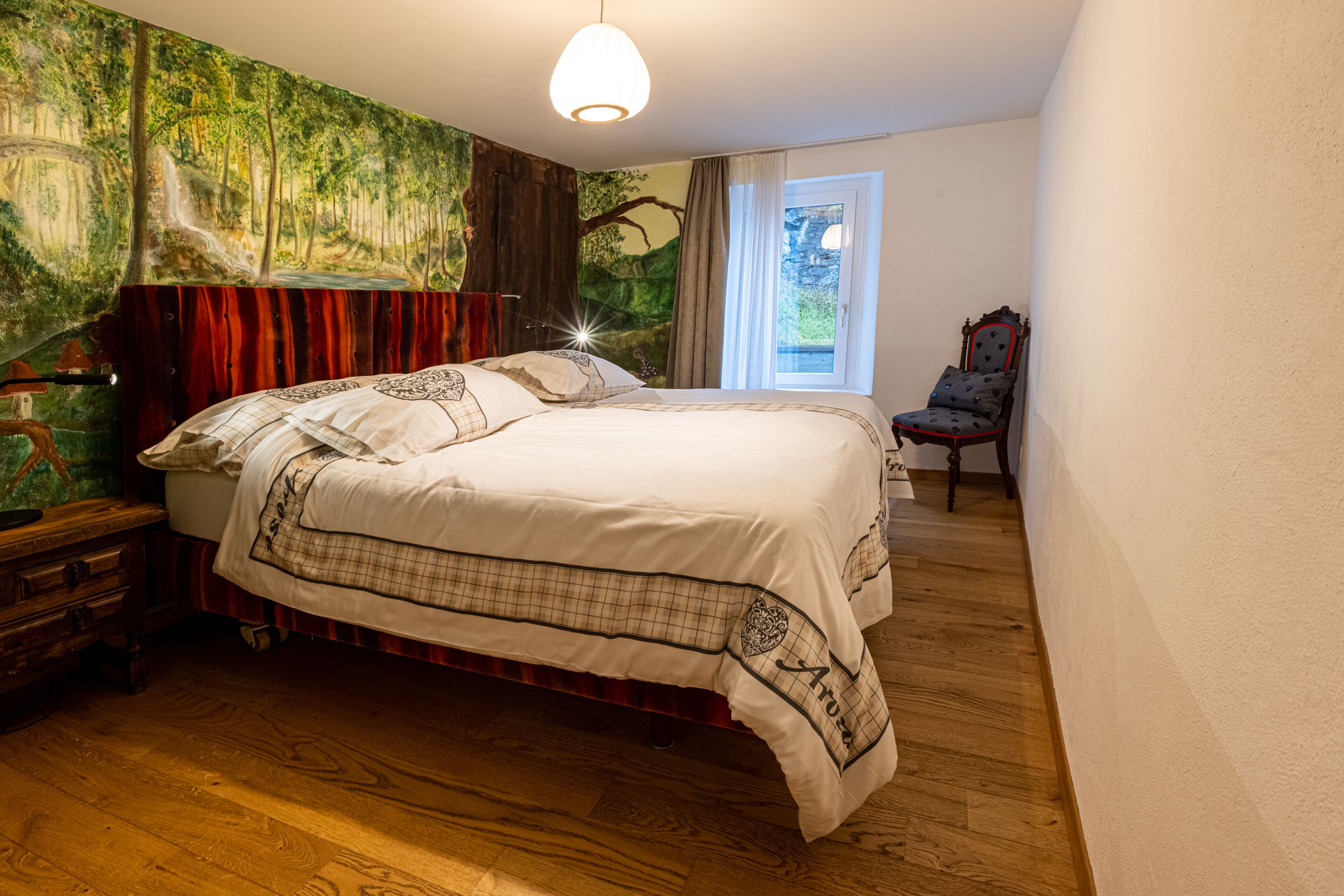 A bedroom with a large bed, a wooden dresser, a chair, and a mural on the wall.