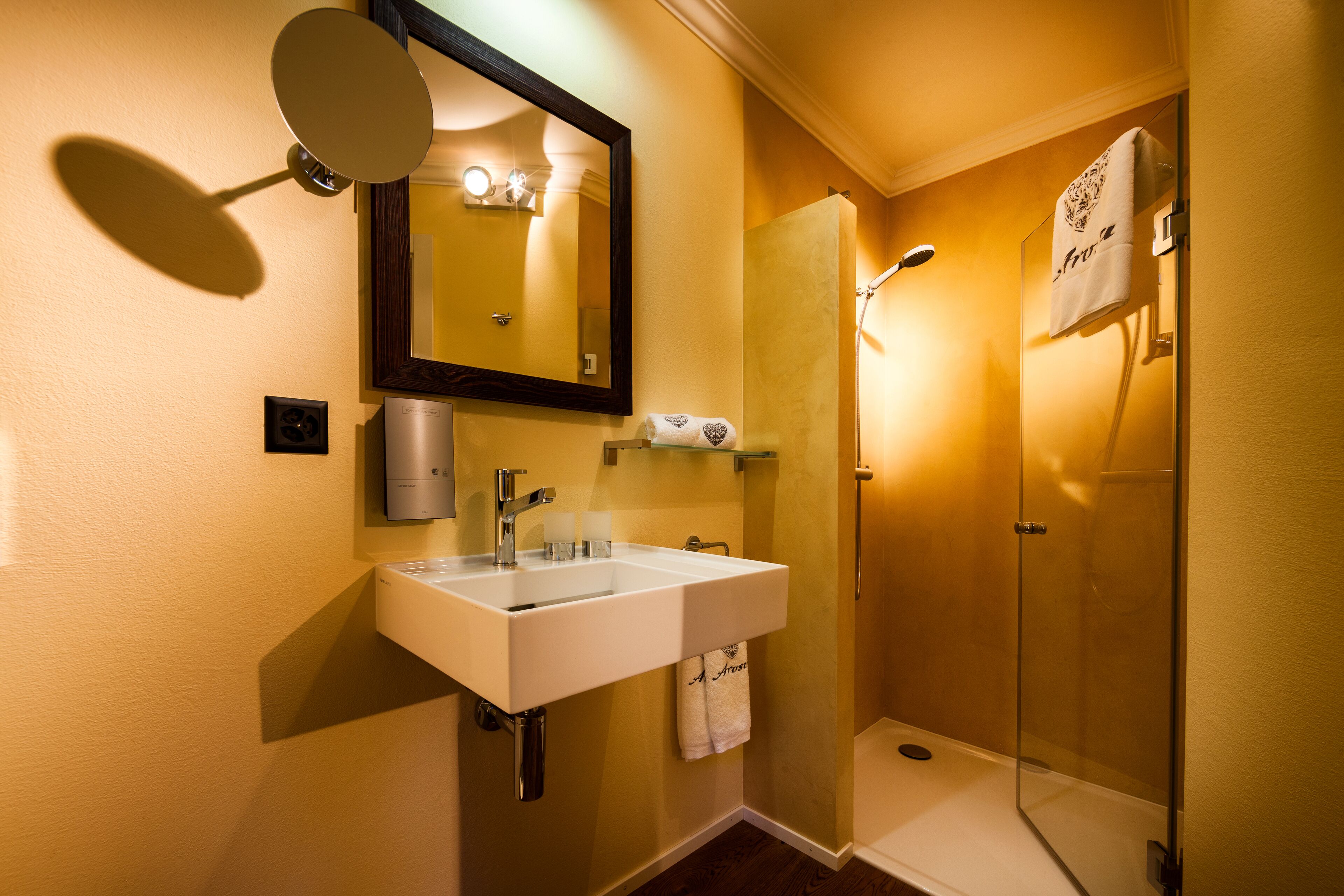 Un baño con lavamanos blanco, espejo, toallero y cabina de ducha acristalada.