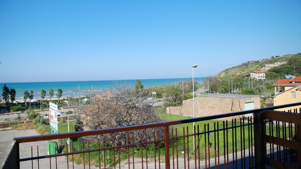 A balcony with a view of a coastal area, including a beach and buildings on a hillside. - Cala Chiara B&B (Ortona)