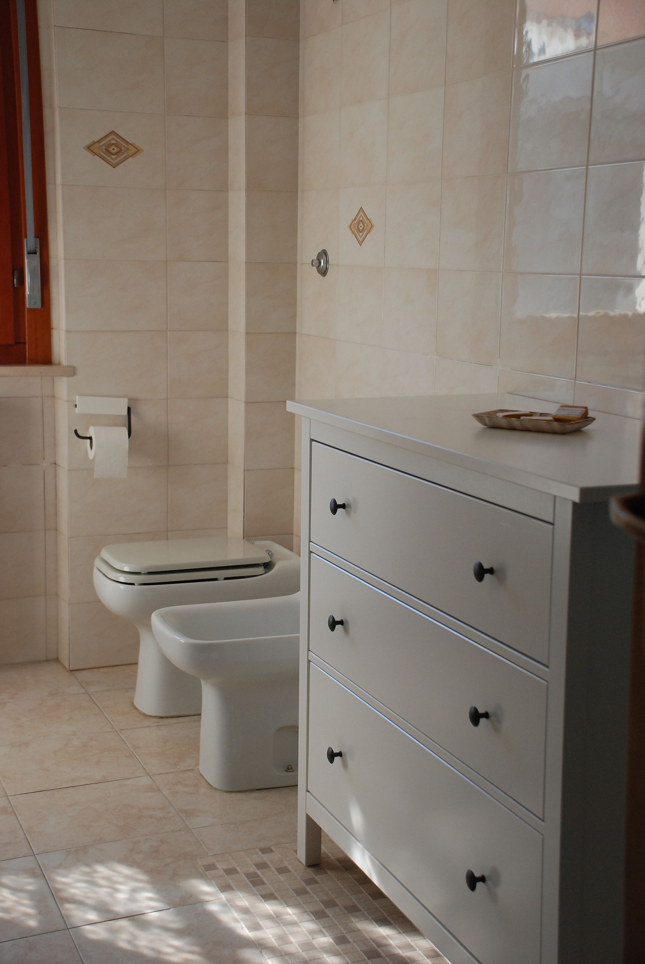 Een badkamer met een toilet, een kast met lades en een betegelde vloer.