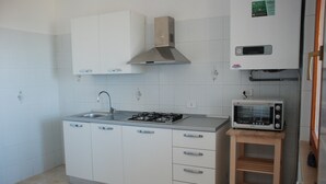 A kitchen with white cabinets, a gas stove, a microwave, and a wooden shelf. - Cala Chiara B&B (Ortona)