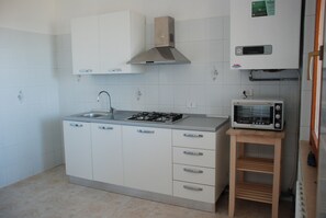 Una cucina con mobili bianchi, un fornello a gas, un forno a microonde e uno scaffale in legno.