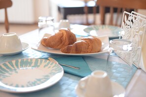 A breakfast setting with croissants, plates, cups, and a napkin on a table. - Cala Chiara B&B (Ortona)