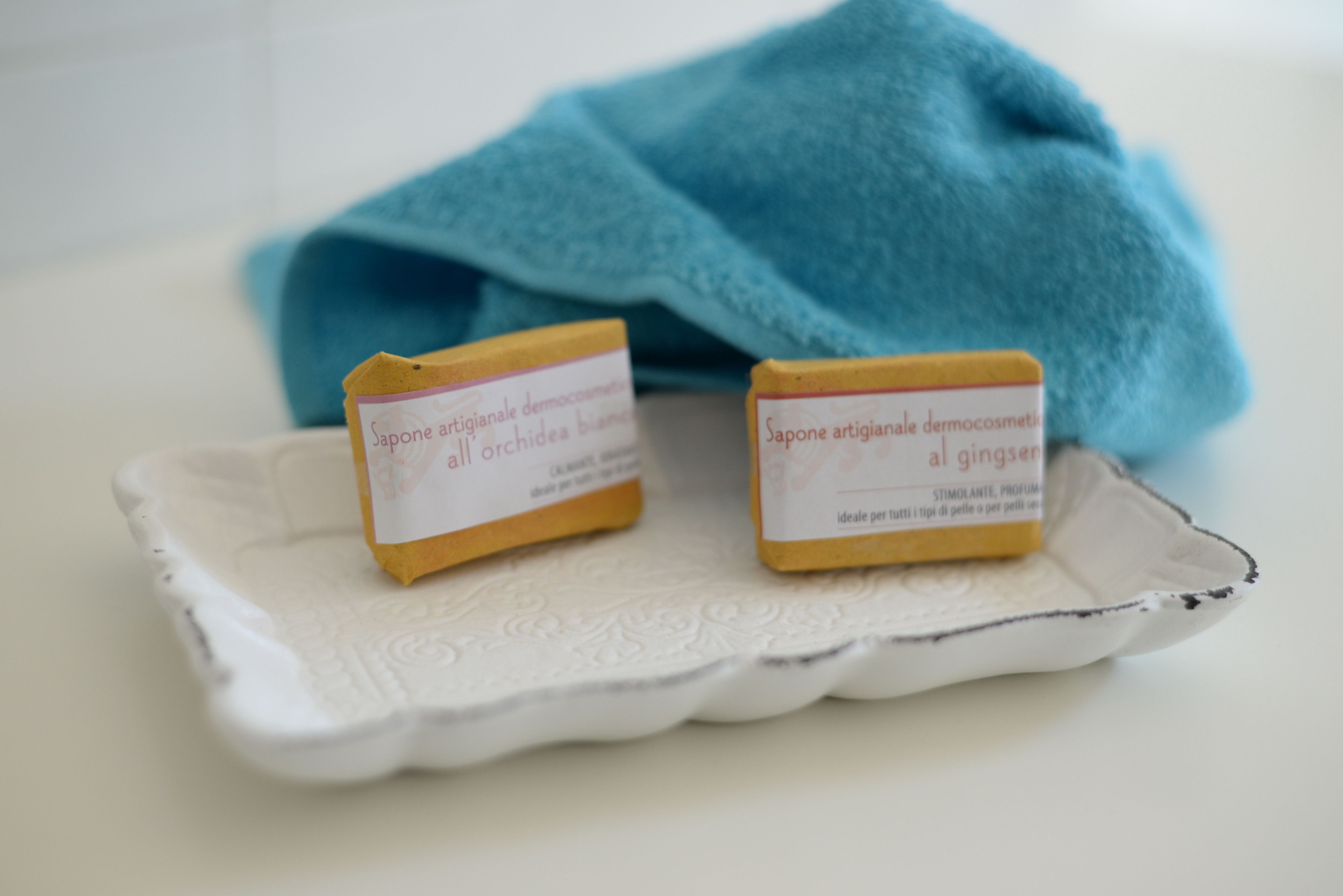 Two small soap bars on a white ceramic dish with a blue cloth in the background.