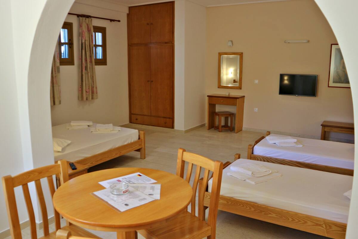 A room with two single beds, a wooden desk with a chair, a small table, and a television.