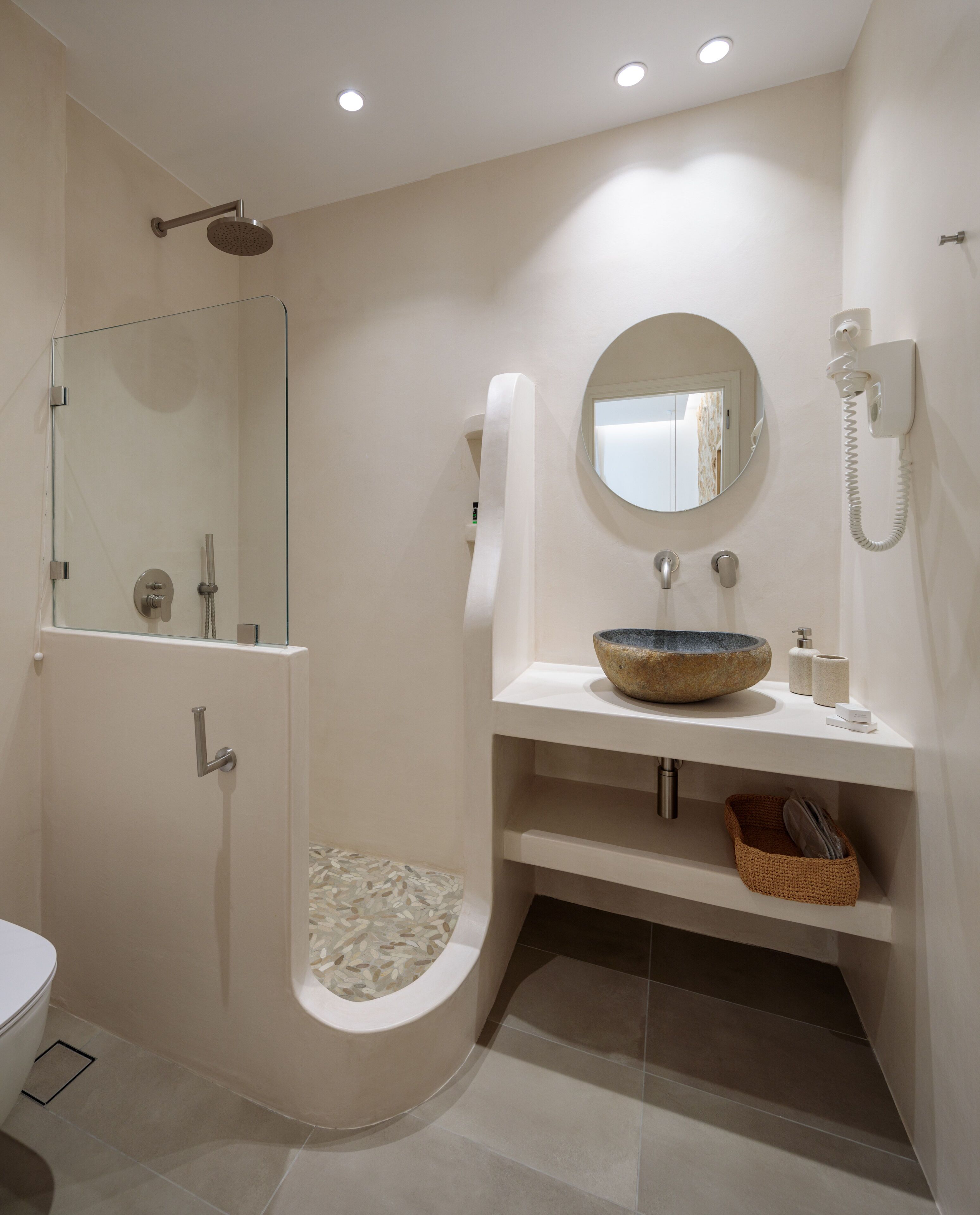 A modern bathroom with a glass-enclosed shower, a round mirror, a sink with a stone basin, and a telephone.
