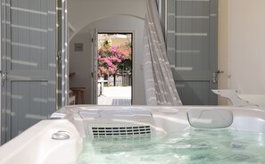 Un bain à remous avec vue sur un jardin et des fleurs roses, visibles à travers une porte ouverte.