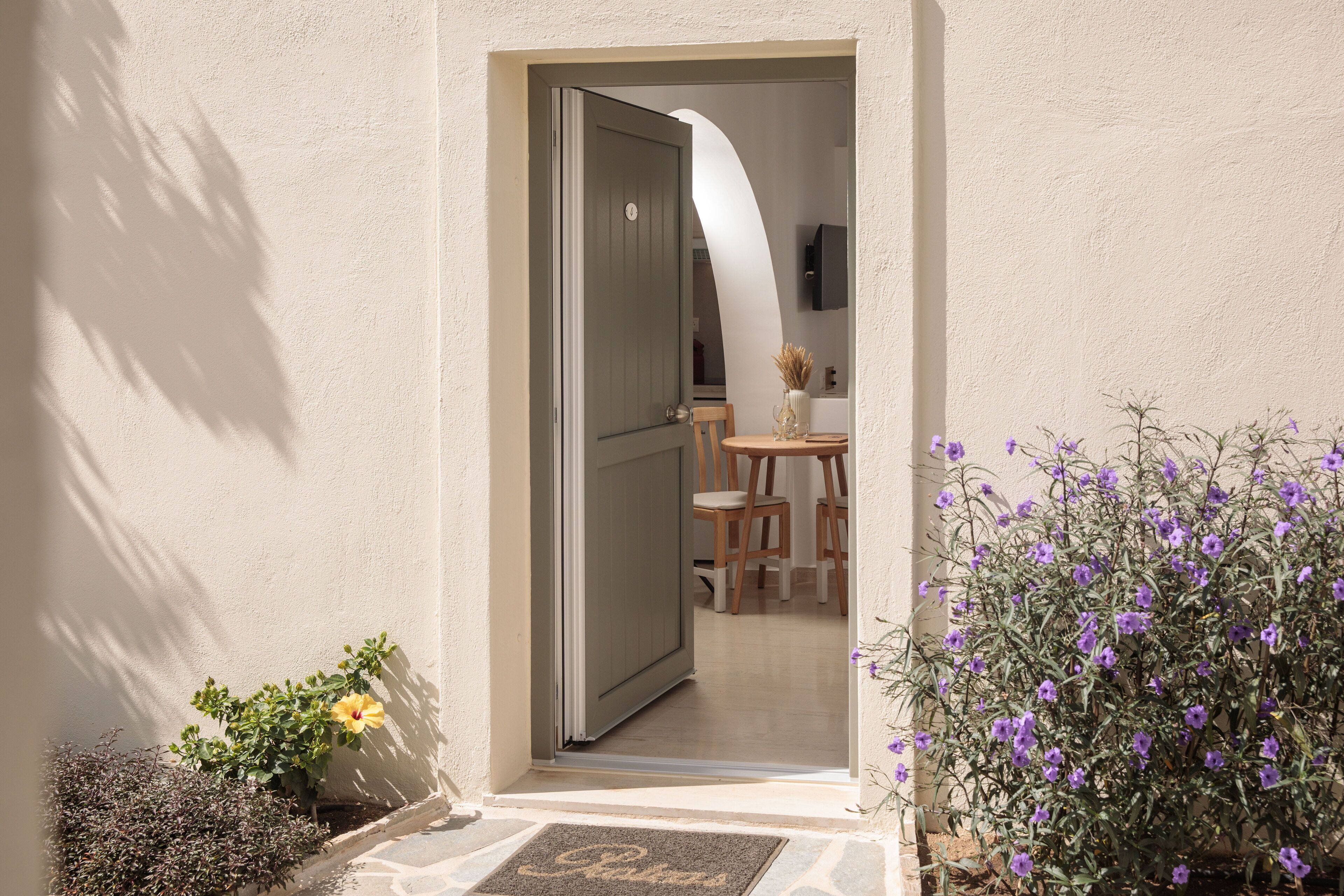 A doorway leading to a room with a dining table and chairs, a small plant, and a door with a number plate.