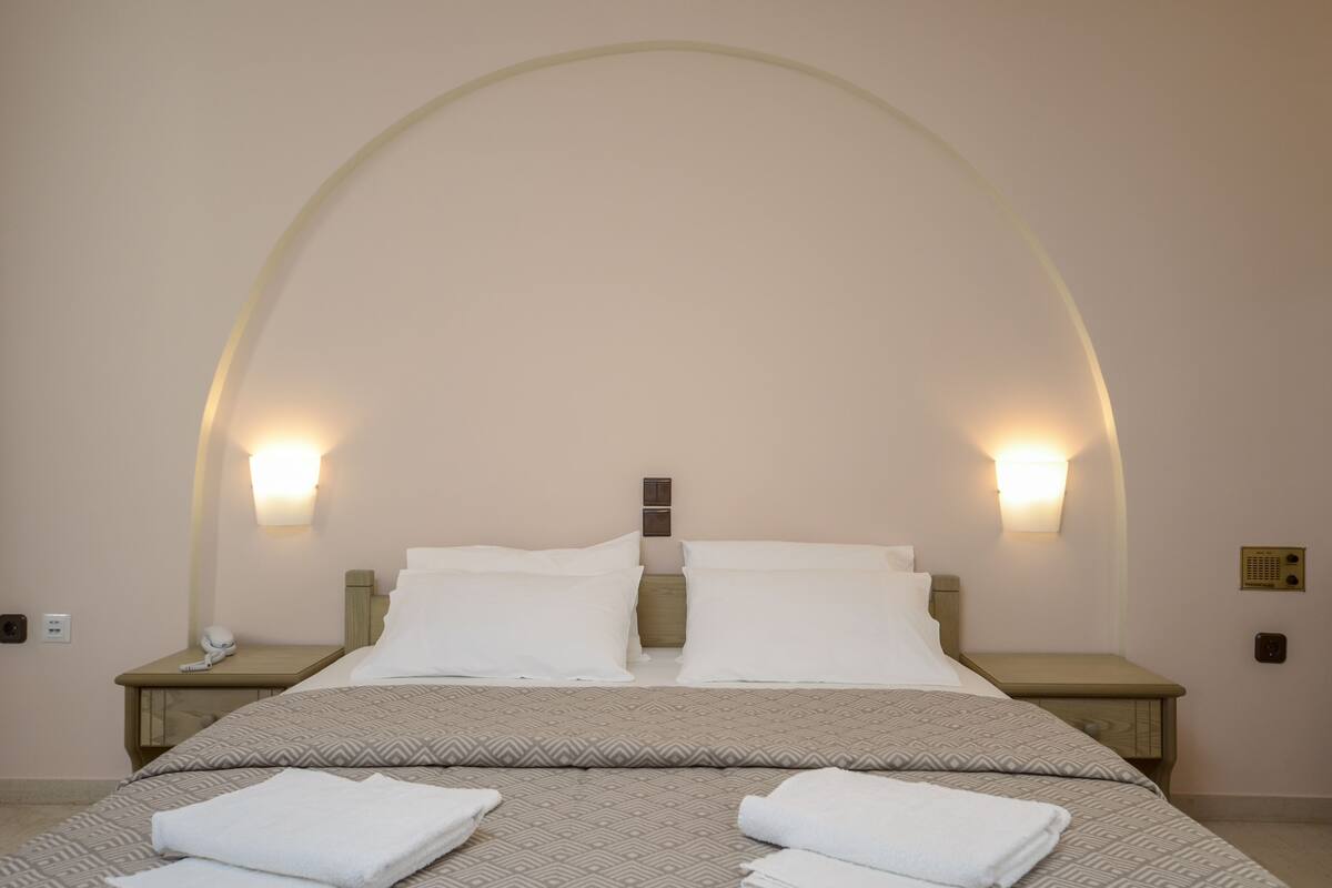 A hotel room with a large bed, two bedside tables, and wall-mounted light fixtures.