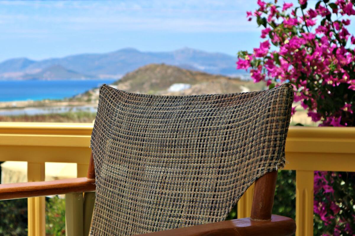 A wicker chair with a view of the sea and mountains in the background.