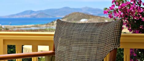 A wicker chair with a view of the sea and mountains in the background.