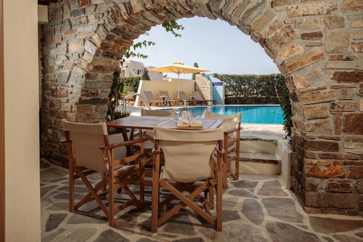 A stone archway leading to a pool area with a table and chairs, a book, and an umbrella.