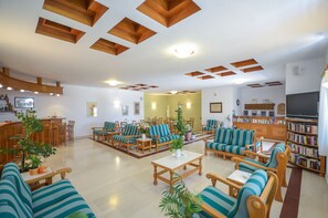A spacious living area with striped sofas, wooden tables, and a bookshelf filled with books. - Proteas Hotel & Suites (Naxos)