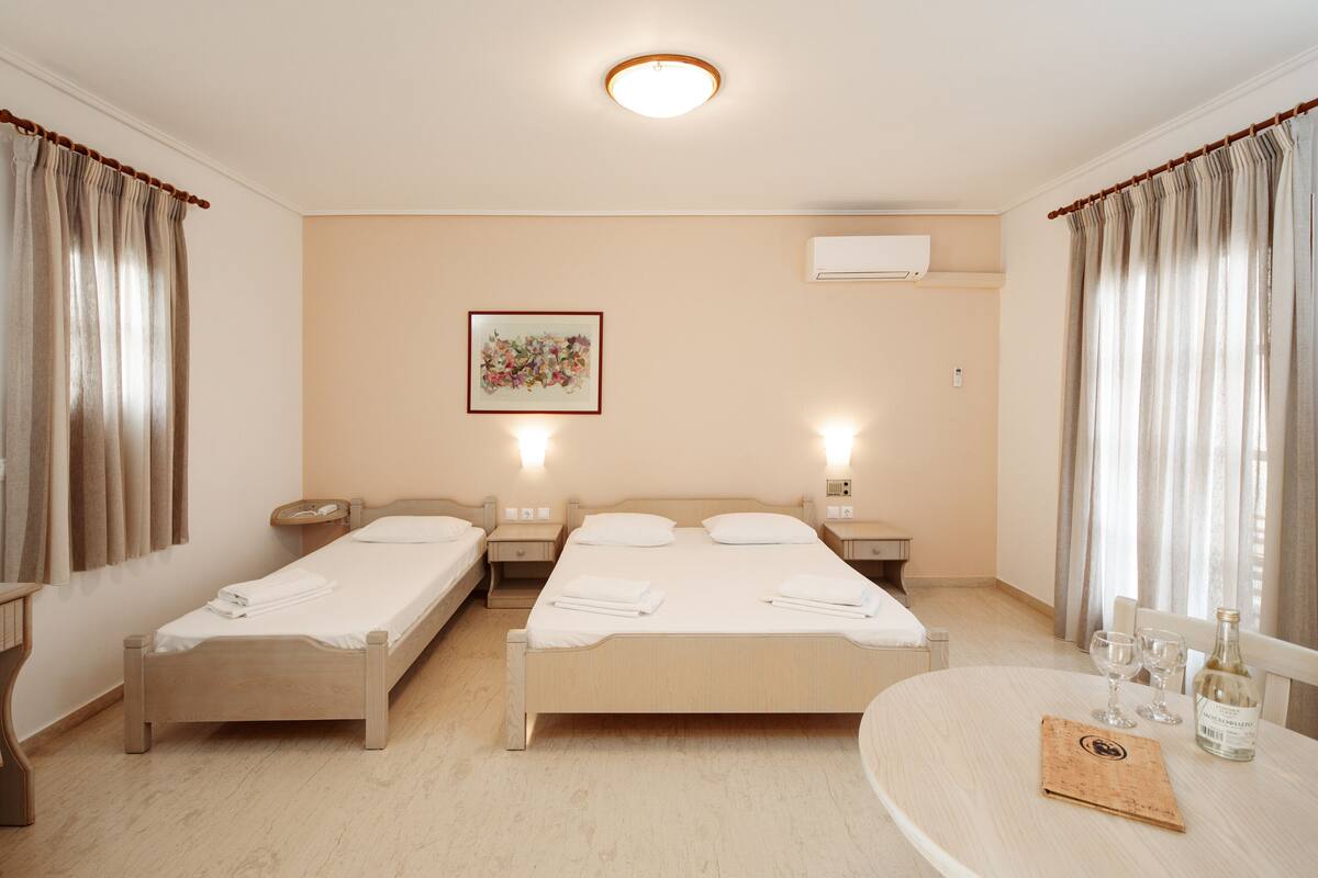 A hotel room with two single beds, a round table with two glasses and a bottle, and a painting on the wall.