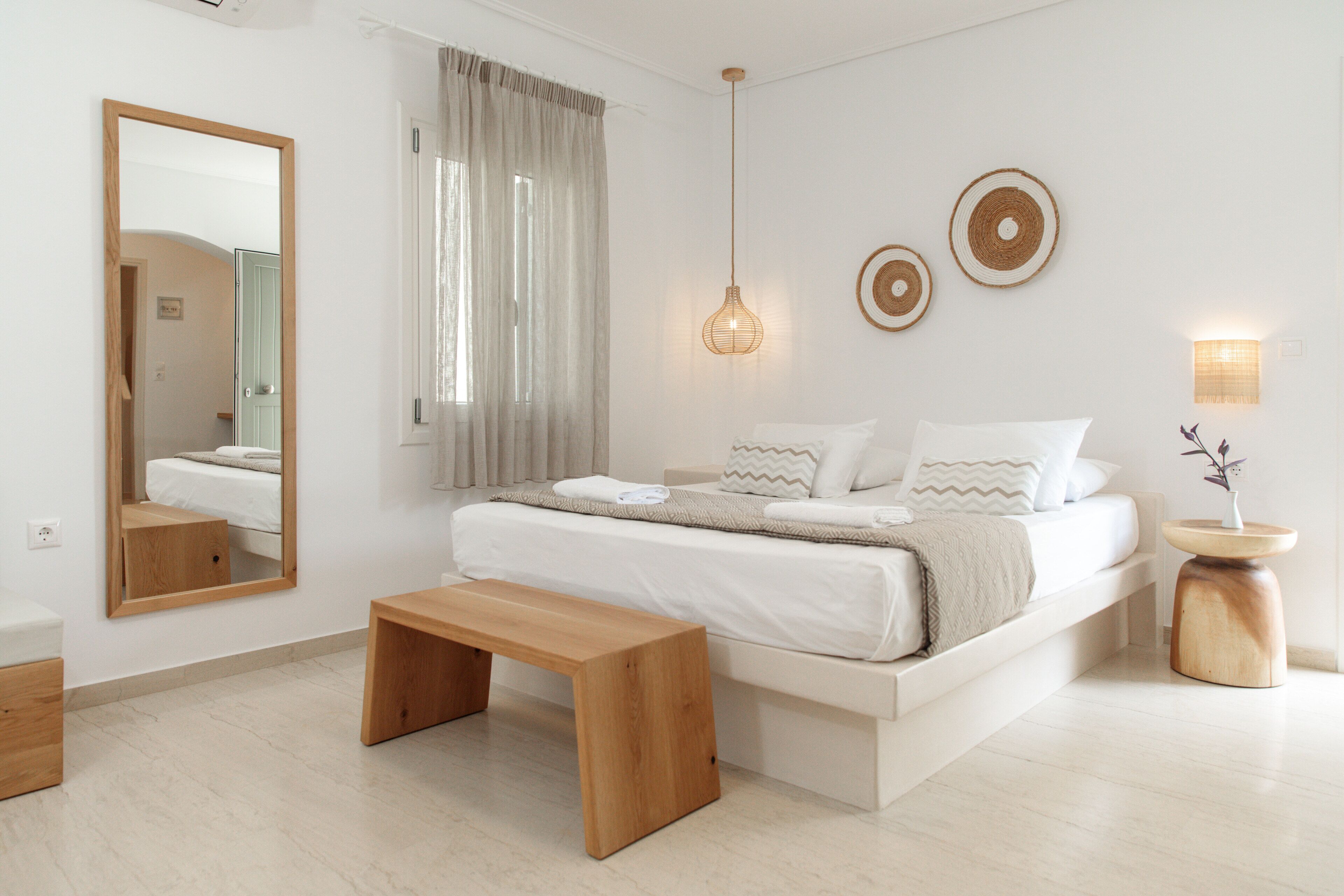 A modern bedroom with a large bed, bedside tables, a bench, and a mirror.