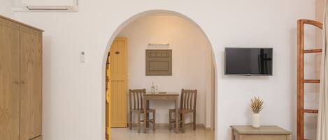 A room with a bed, a wooden wardrobe, a dining table with chairs, a television, and a small table with a plant.