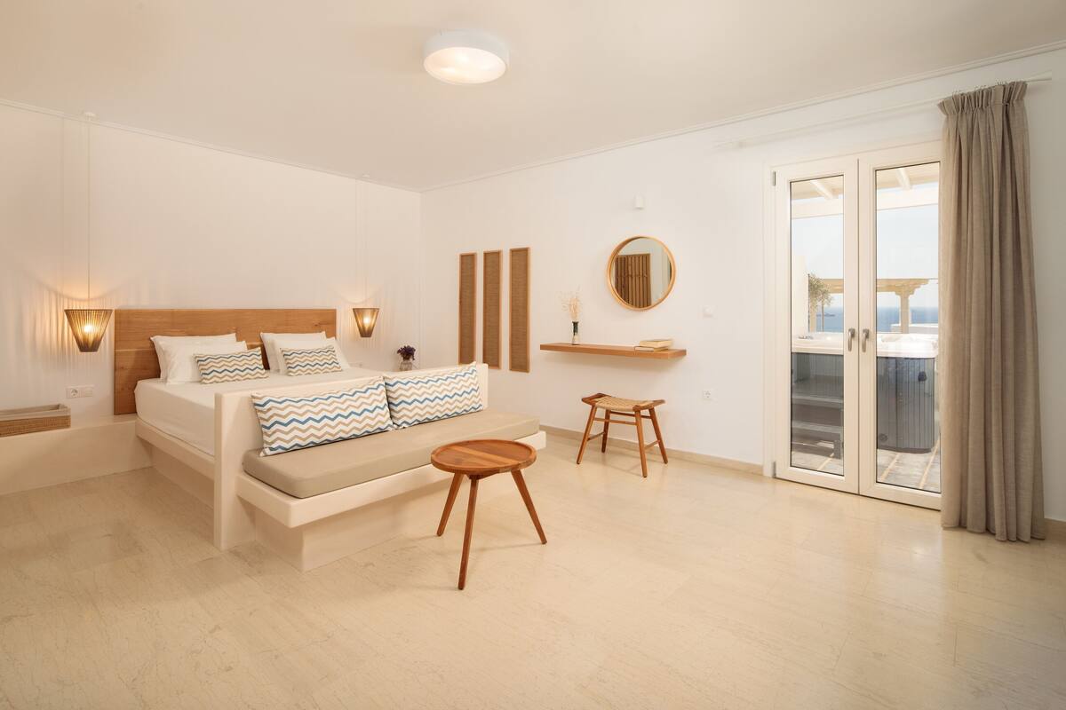 A modern bedroom with a bed, bedside tables, a sofa, a mirror, and a view of the outdoors.
