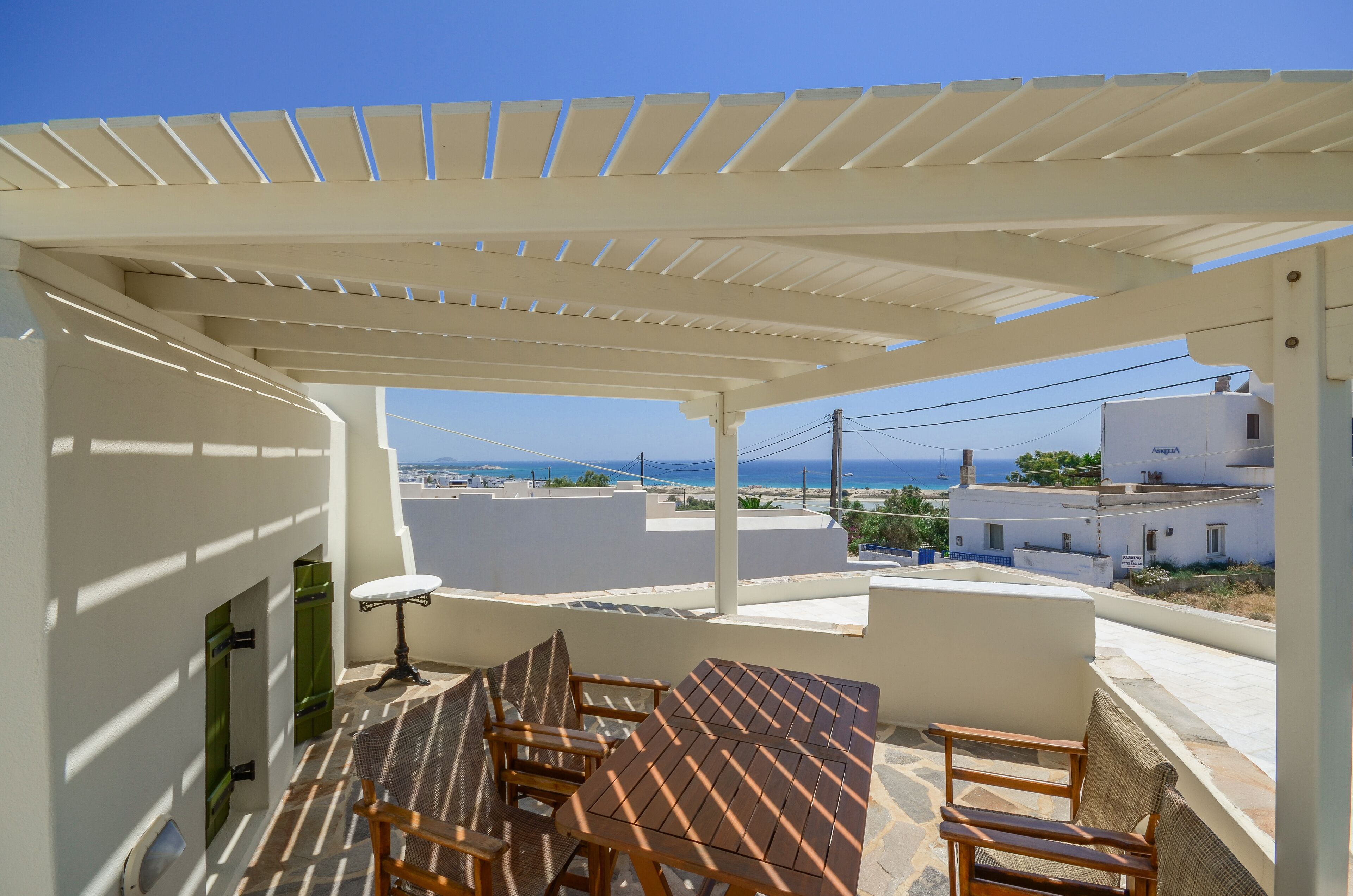 A terrace with a table and chairs, a pergola, and a view of the sea and buildings.