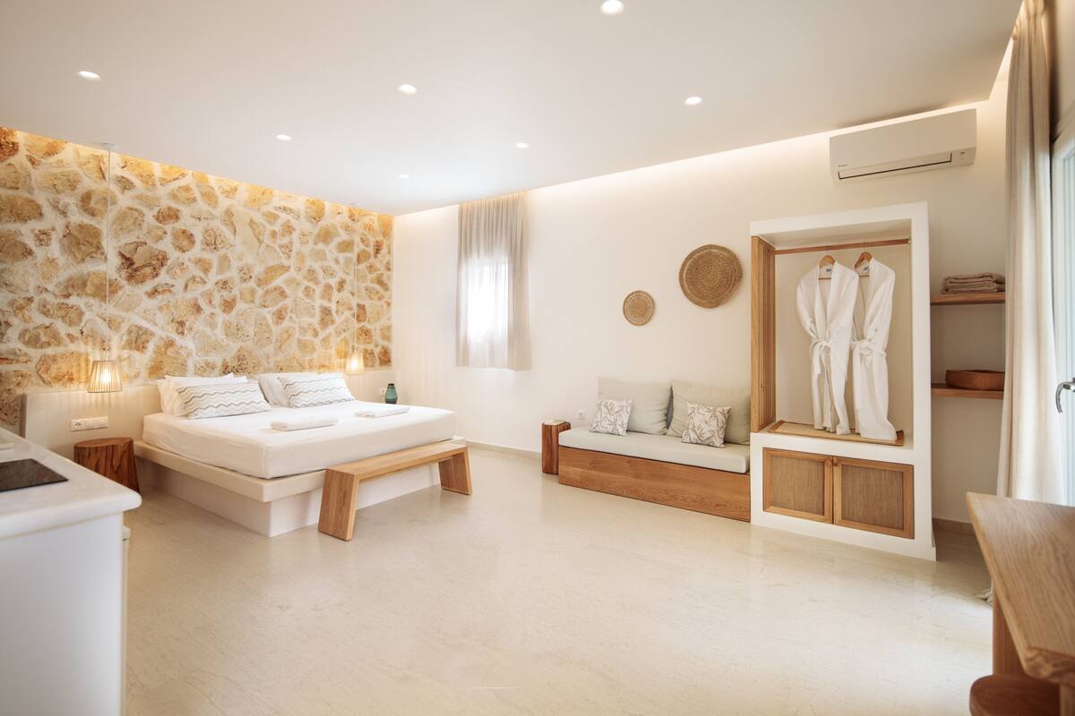 A modern bedroom with a stone accent wall, a bed, a sofa, a robe rack, and a small wooden table.