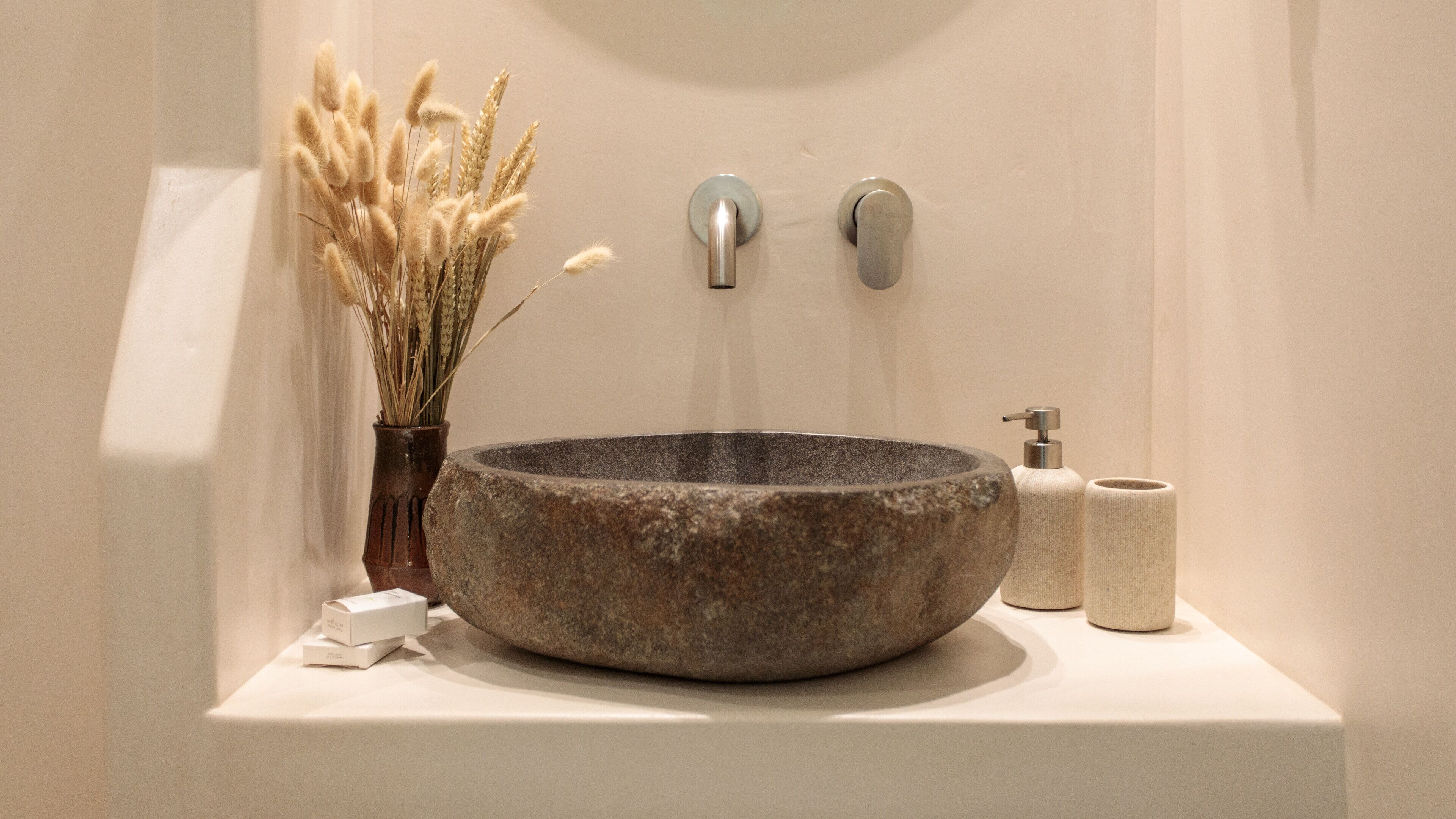 A stone basin sink with a faucet and soap dispenser on a white countertop.