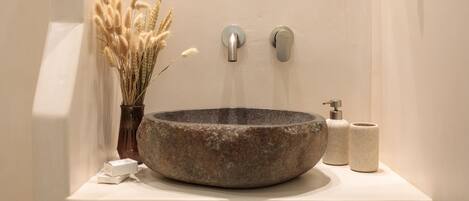 A stone basin sink with a faucet and soap dispenser on a white countertop.