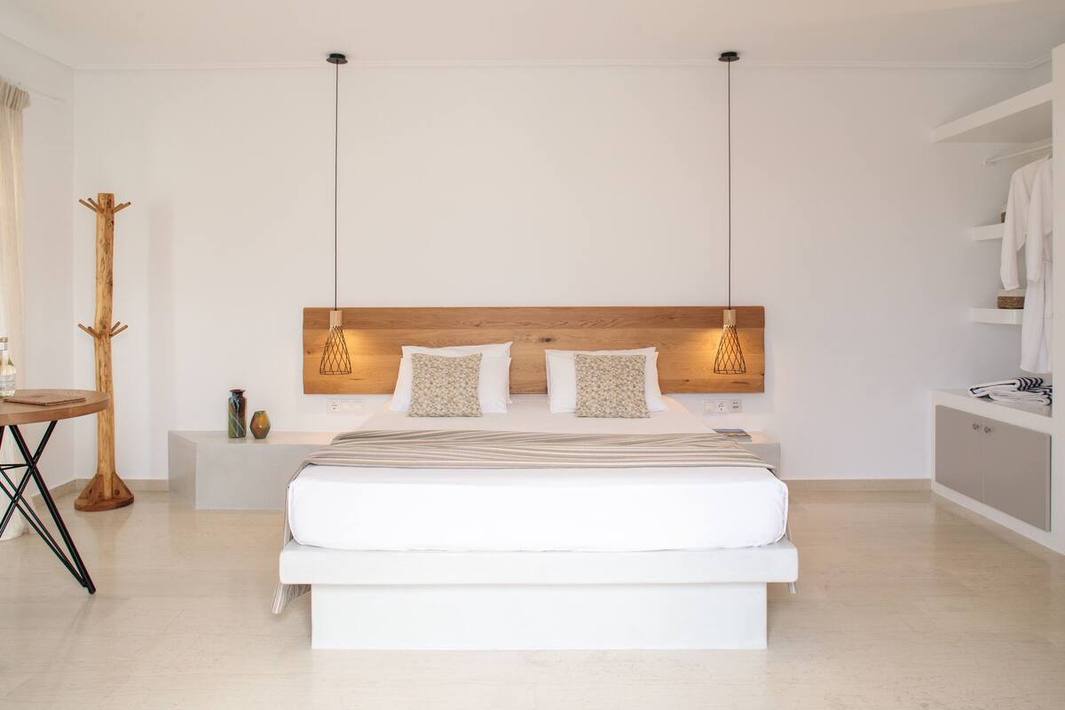A modern bedroom with a large bed, bedside tables, a coat rack, and a wardrobe.