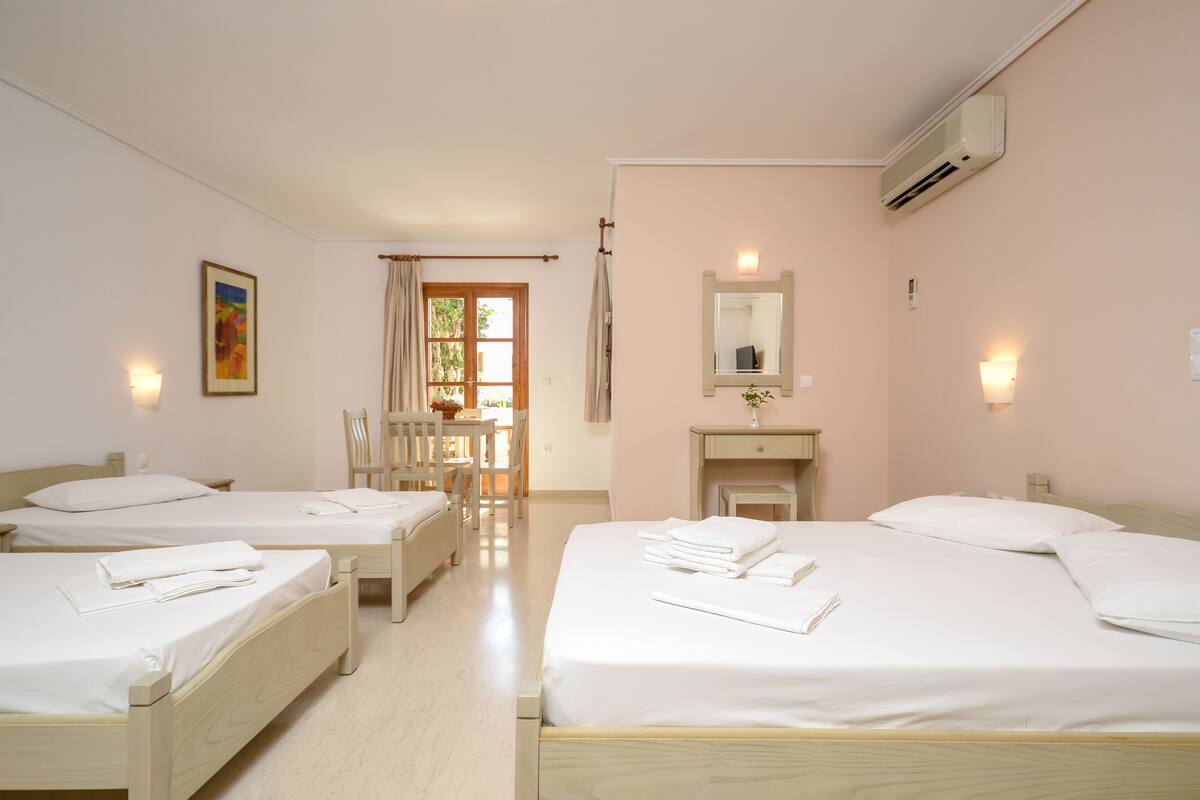 A hotel room with two single beds, a wooden chair, a small table, a mirror, and a window with curtains.