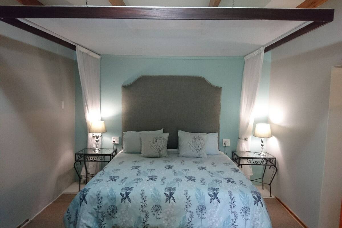 Une chambre à coucher avec un lit à baldaquin, deux tables de chevet avec des lampes et une couvre-lit à motifs floraux.