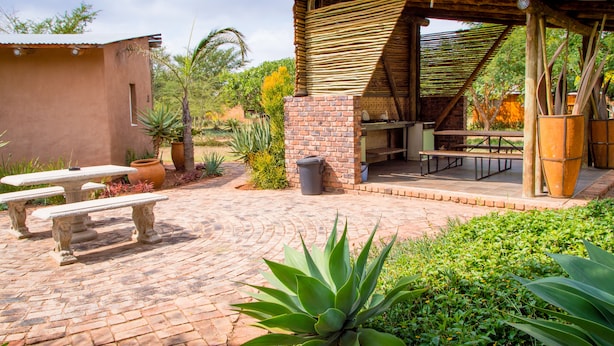 An outdoor patio with stone tables, a brick barbecue area, and potted plants. - Destiny Inn Lodge (Polokwane)