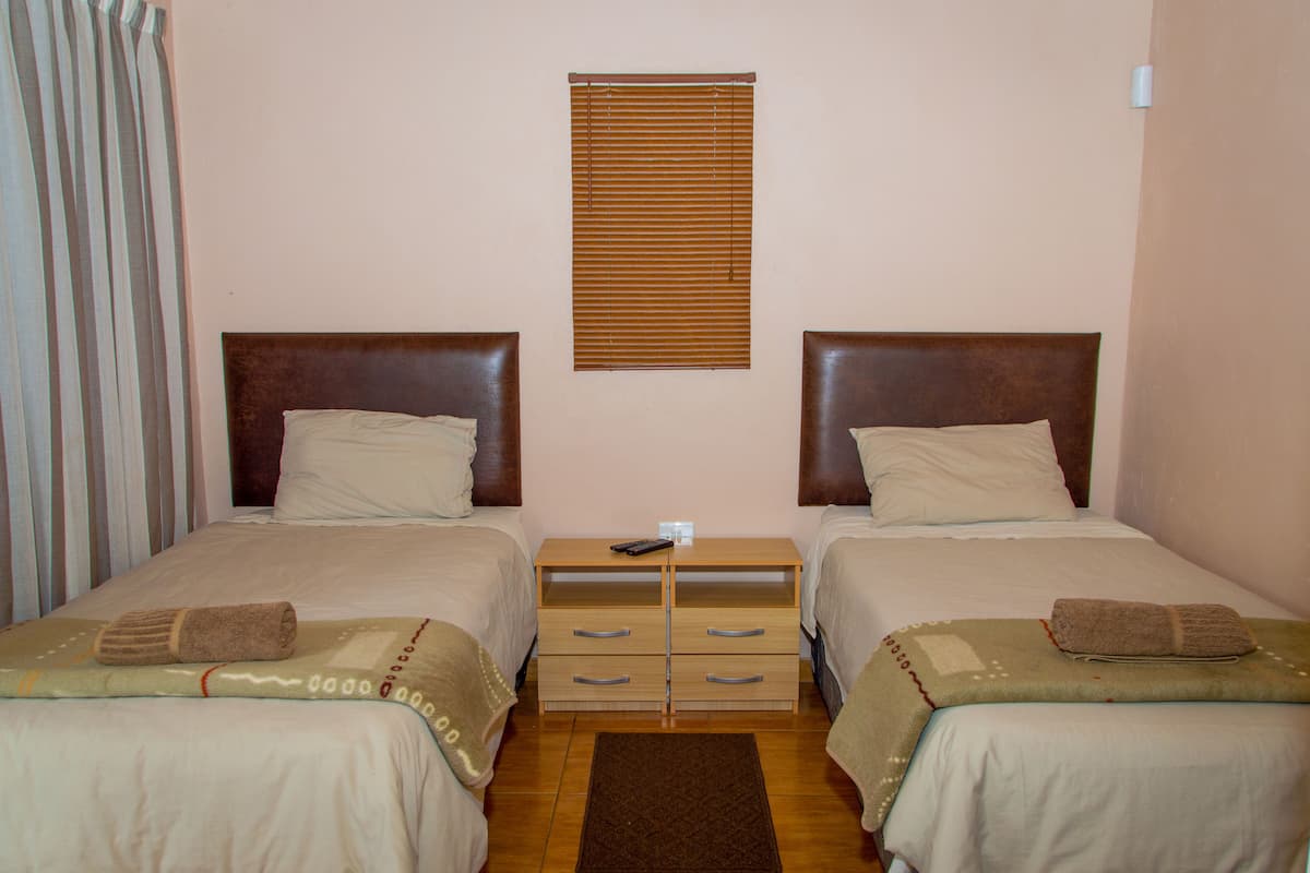 Une chambre double avec deux lits, une table de chevet en bois et une fenêtre avec des stores.