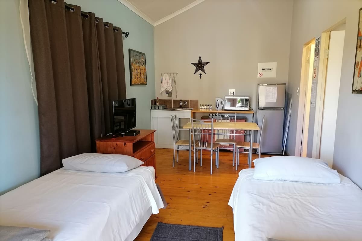 Une chambre avec deux lits simples, un bureau avec une chaise, une télévision, une décoration sur le thème des étoiles et une kitchenette.