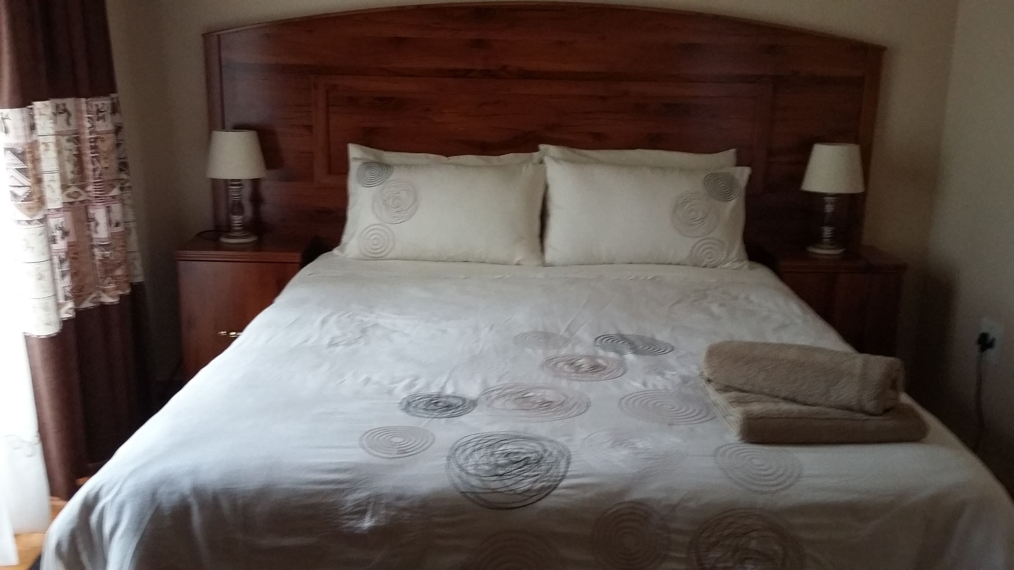 Una cama bien hecha con una colcha estampada, dos lámparas de noche y un cabecero de madera.